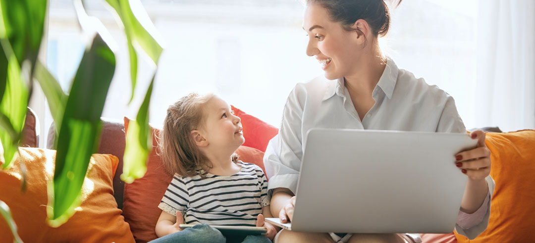 Mujer sosteniendo un ordenador y sonriendo a su hija que está al lado de ella con una tablet